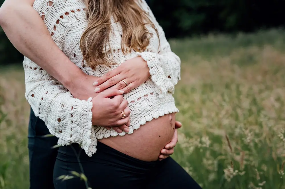 Schwangere hält ihren Babybauch auf einer Wiese