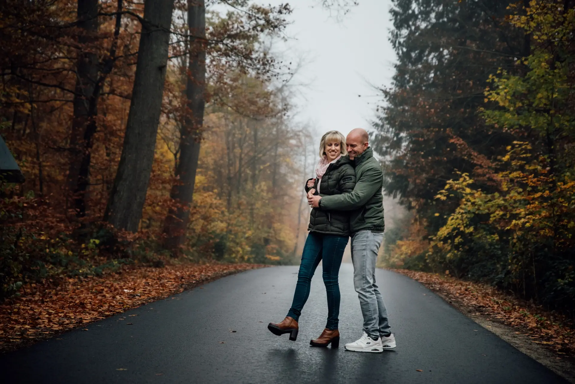 Paar umarmt sich lachend auf einer herbstlichen Waldstraße