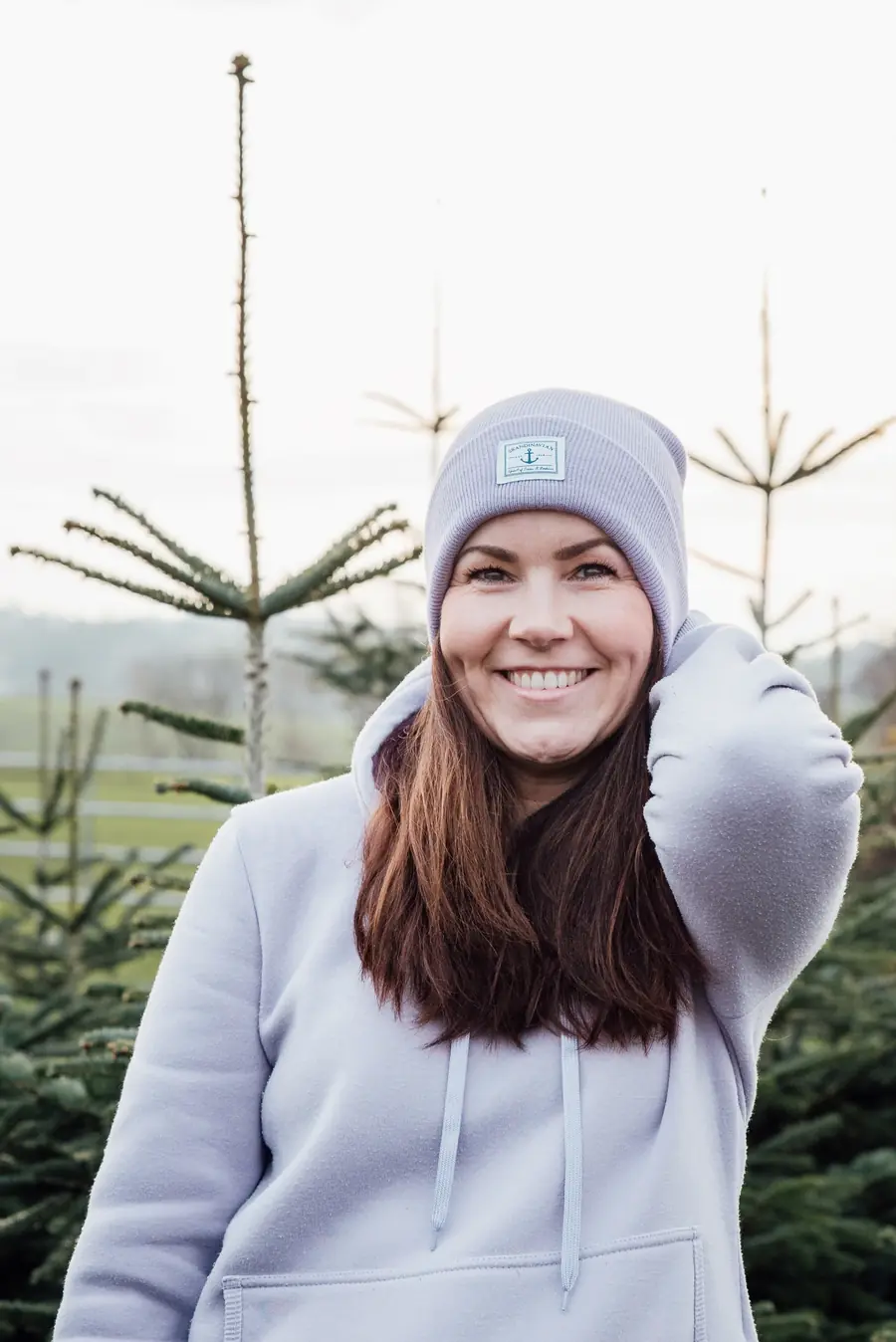 Simone Becker lächelnd in lila Mütze zwischen jungen Tannen